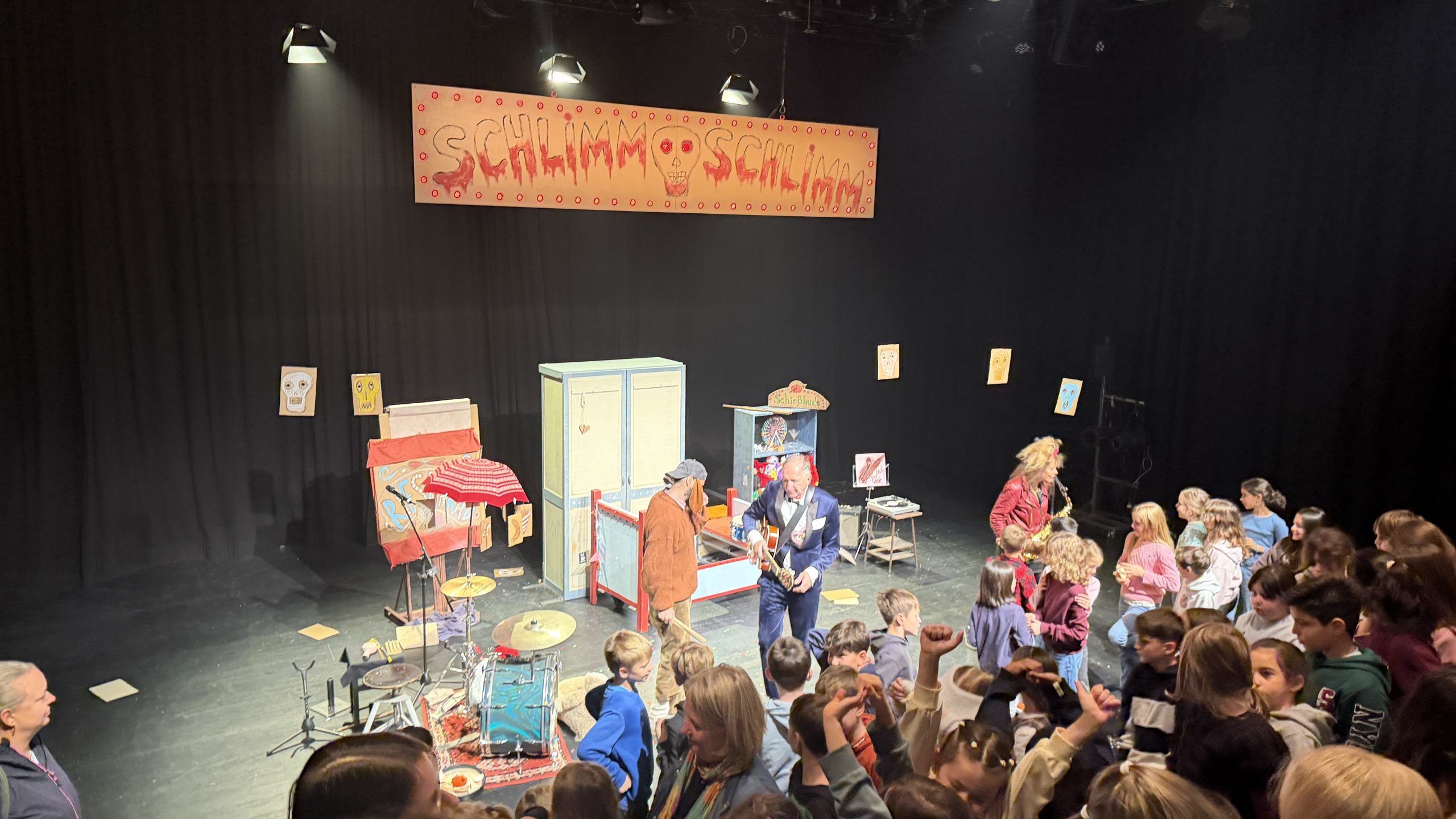 Bühnenbild des Theaterstücks Schlimm schlimm mit beleuchtetem Schriftzug und Requisiten